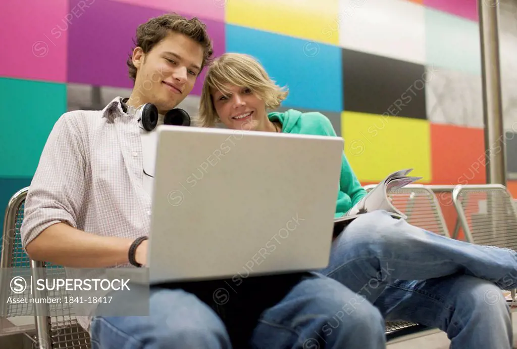Teenager couple using laptop at underground station, low_angle view