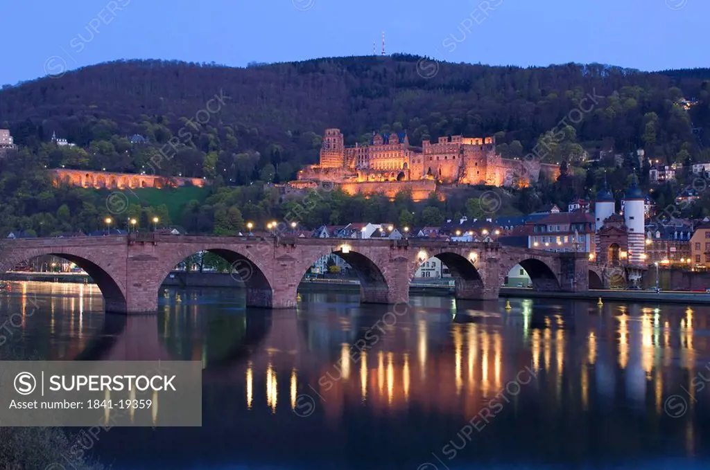 Arch bridge across river lit up at dusk, River Neckar, Heidelberg, Germany