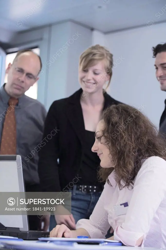 Businesswomen and businessmen looking at laptop and smiling