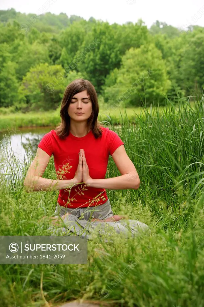 Woman practising yoga by a pond, front view