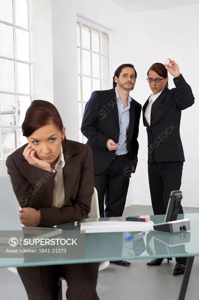 Businesswoman looking bored with two businesspeople standing in background