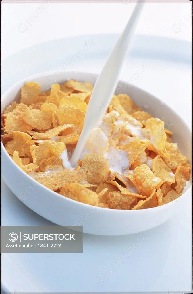 Close_up of bowl of corn flakes with milk being poured