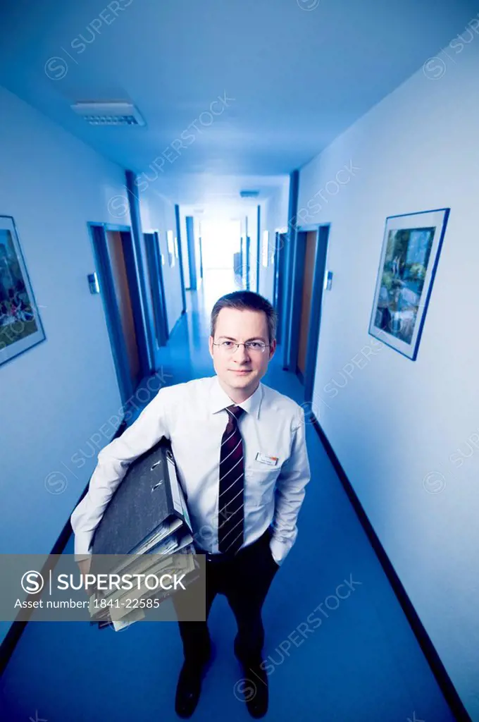 Businessman standing in an office corridor, holding files, front view