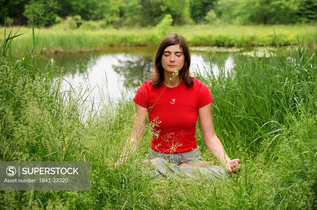 Woman meditating by a pond, front view