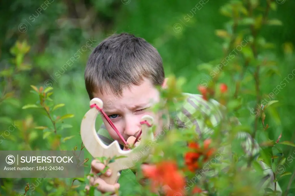 boy with slingshot in garden, aiming