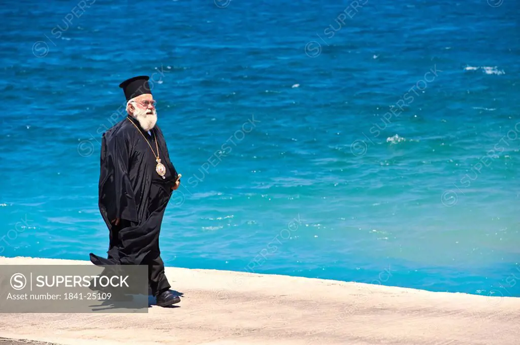 Orthodox priest strolling on waterside promenade, Kalymnos, Greece