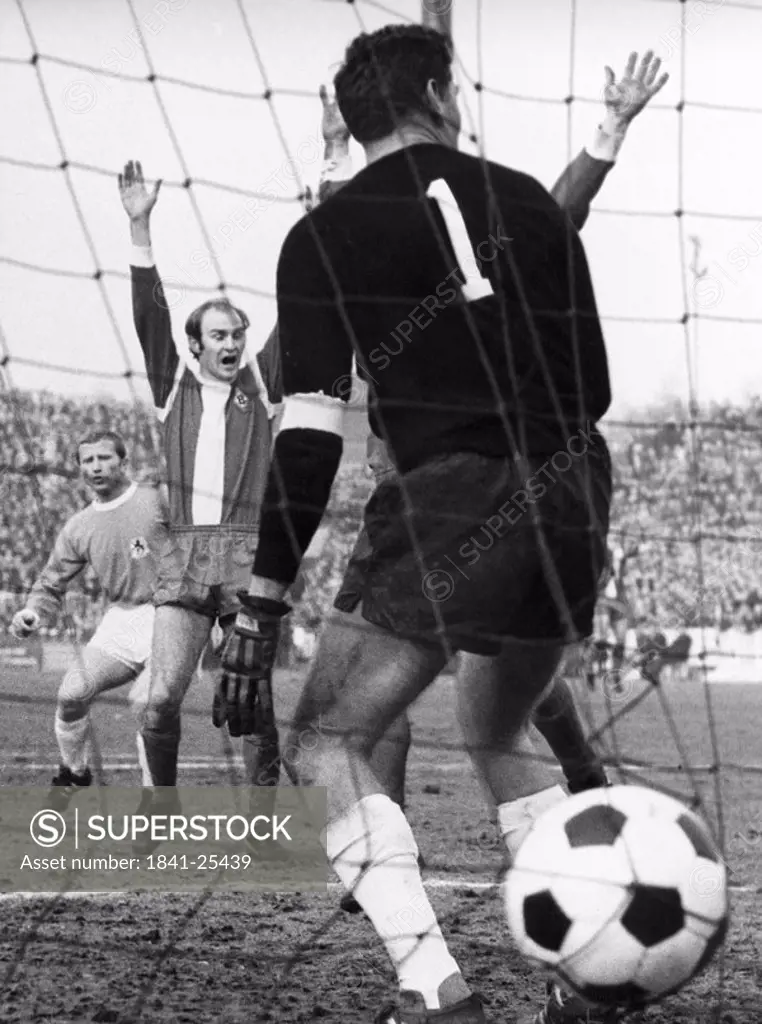 Soccer ball in net with referee raising hands in background, Germany