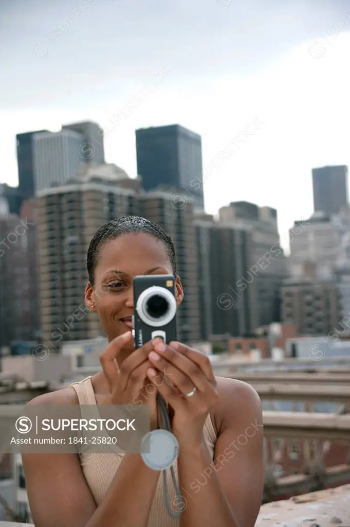 Woman taking picture with a camera, skyline of New York in the background, USA