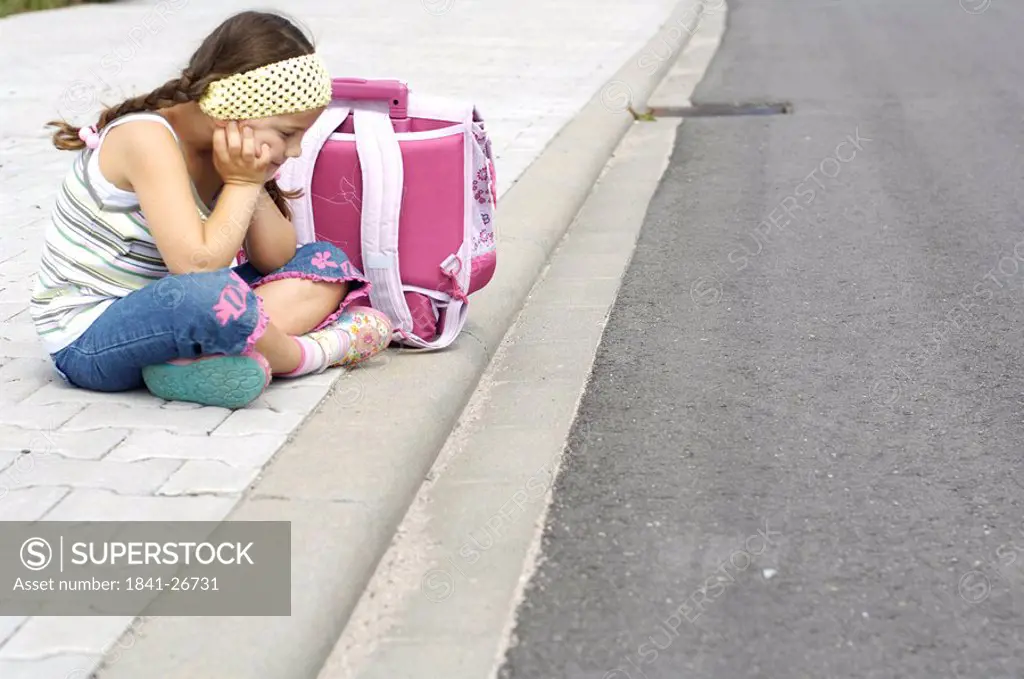 Side profile of girl sitting with schoolbag at roadside