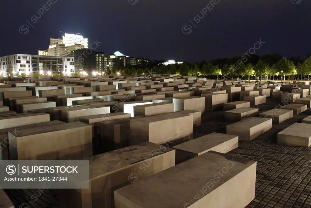 Concrete steles at memorial with building lit up at night in background, Holocaust Memorial, Berlin, Germany