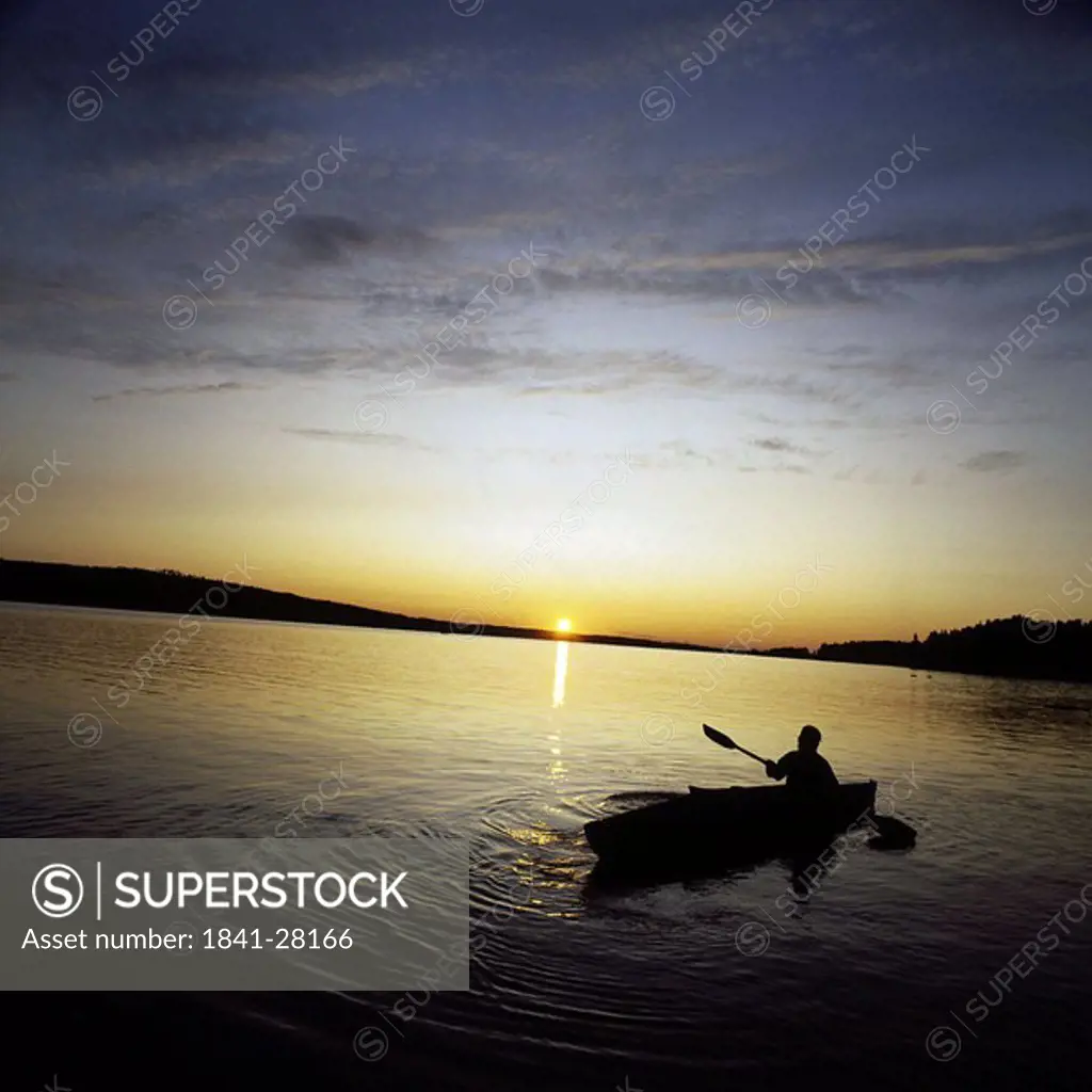 Silhouette of person boating in river at dusk