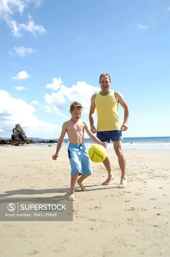 Father playing soccer with his son on beach