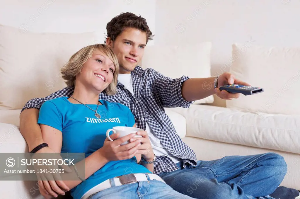 Teenager couple sitting in front of couch and watching television, horizontal format