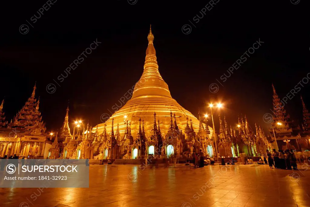 Group of people at Buddhist temple lit up during dusk, Shwedagon Pagoda, Yangon, Myanmar