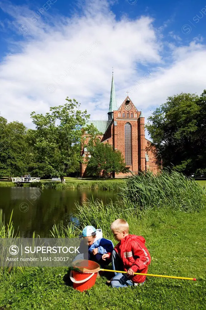 Two children playing at pond side with church in background, Bad Doberan, Mecklenburg_West Pomerania, Germany