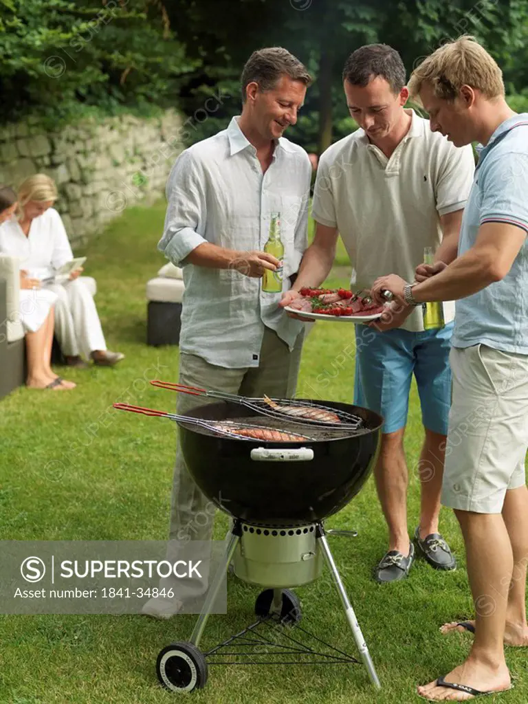 Three men preparing fish on barbeque grill in garden