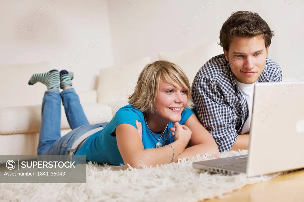 Teenager couple lying on carpet, watching media on notebook, low_angle view