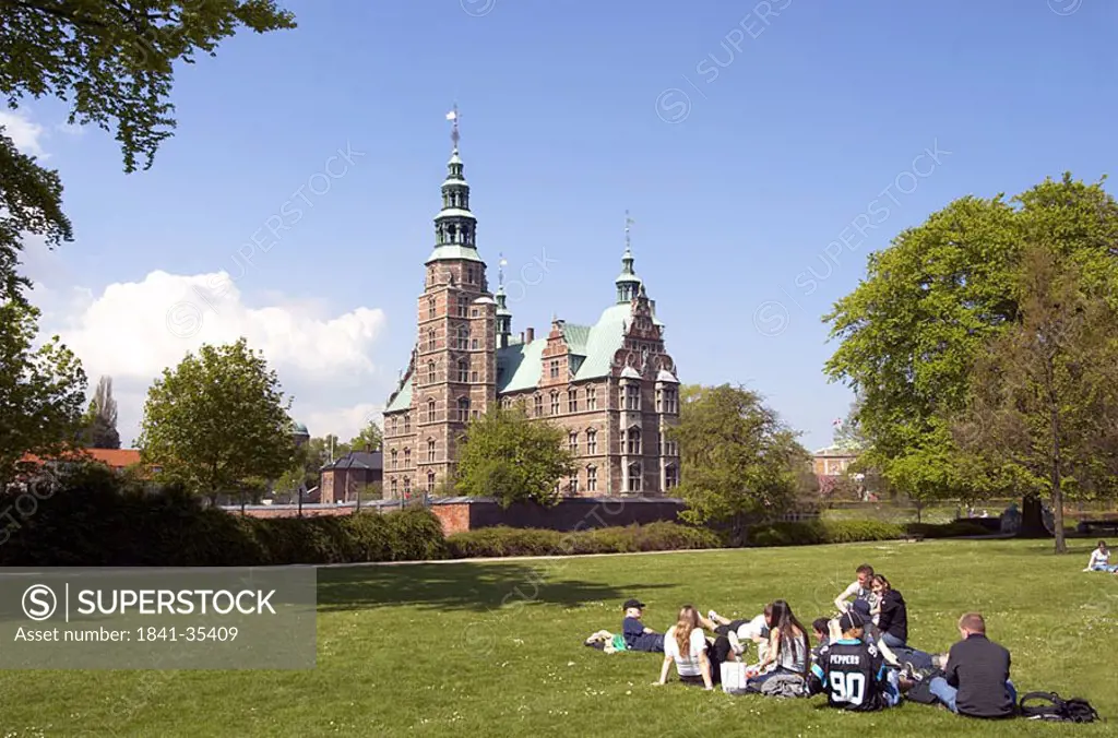Tourists resting in park with castle in background, Rosenborg Castle, Copenhagen, Denmark
