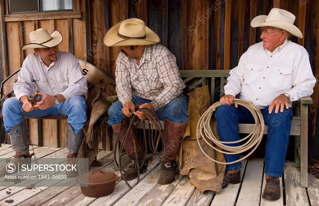 Three cowboys sitting side by side, full shot, USA
