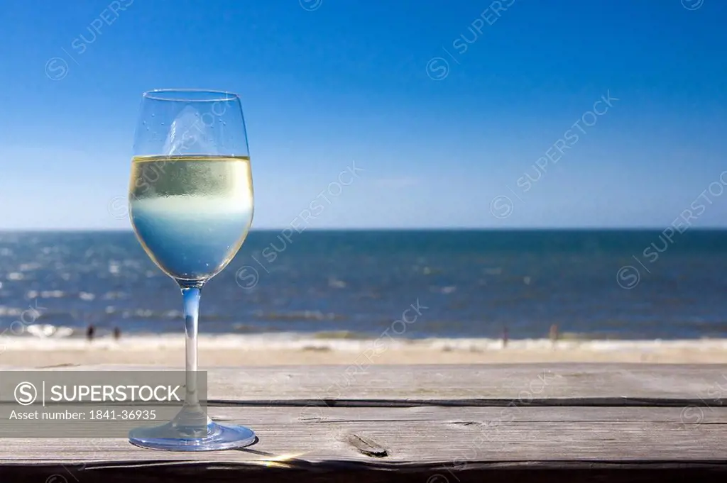 Glas of white wine on wooden board in front of sea, Wenningstedt_Braderup, Sylt, Germany