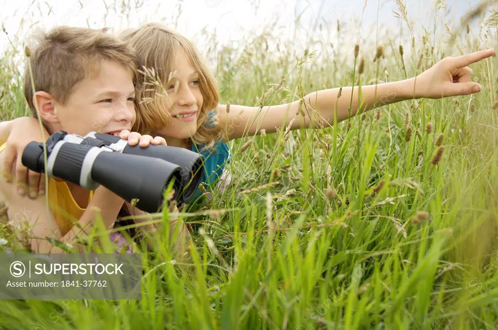 Boy holding binoculars in field with his friend beside him