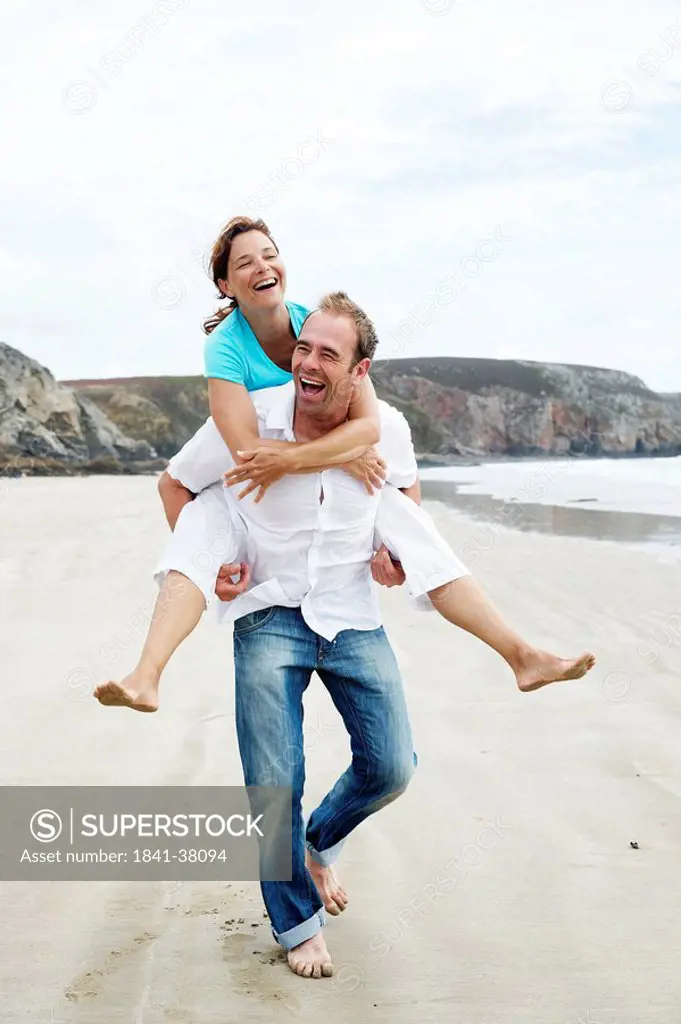 Man giving woman a piggyback ride on the beach, front view