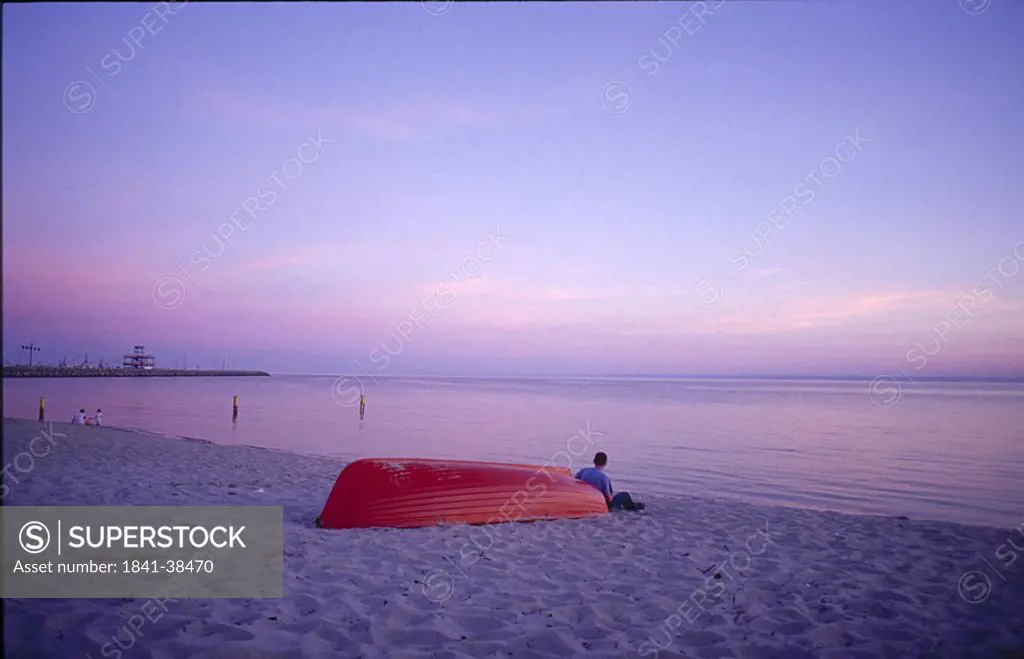 Person sitting leaning against boat on beach, Poland