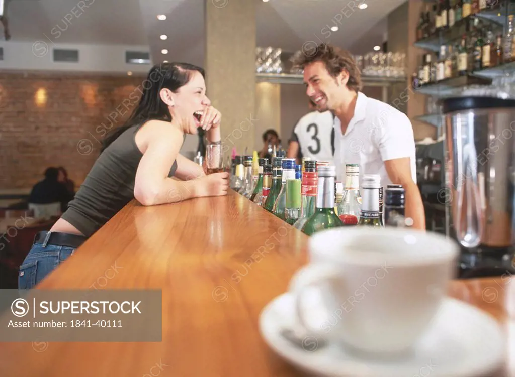 Side profile of young woman and bartender laughing at bar counter
