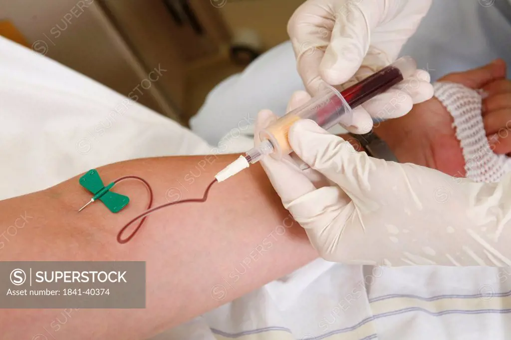 Close_up of person´s hands taking blood sample from patient´s arm