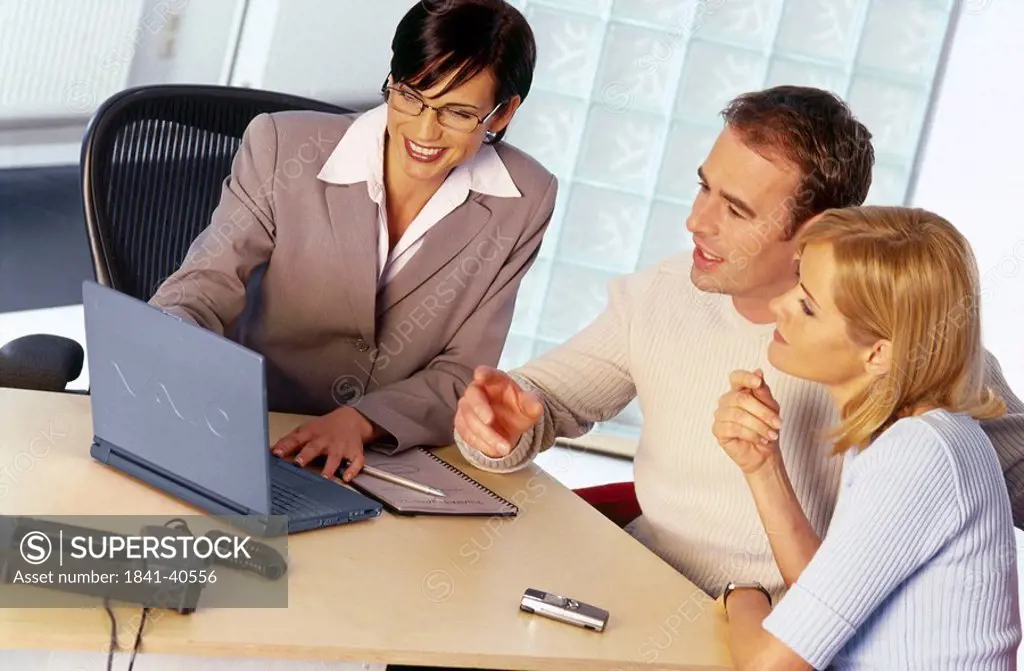 Businesswoman and a young couple looking at a laptop