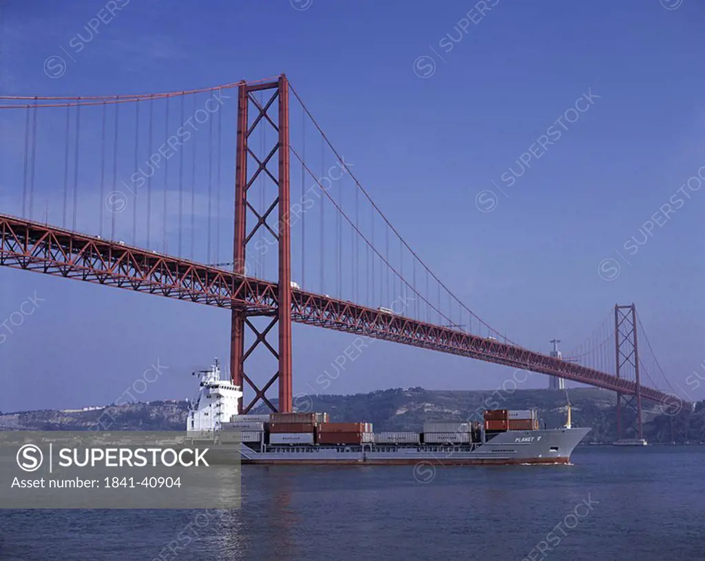 Cargo ship in river under suspension bridge, Belem, Lisbon, Portugal