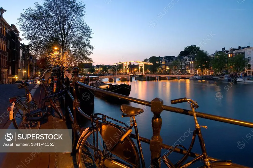 Bicycles parked at riverbank with bridge in background, Magere Brug, Amstel River, North Holland, Amsterdam, Netherlands