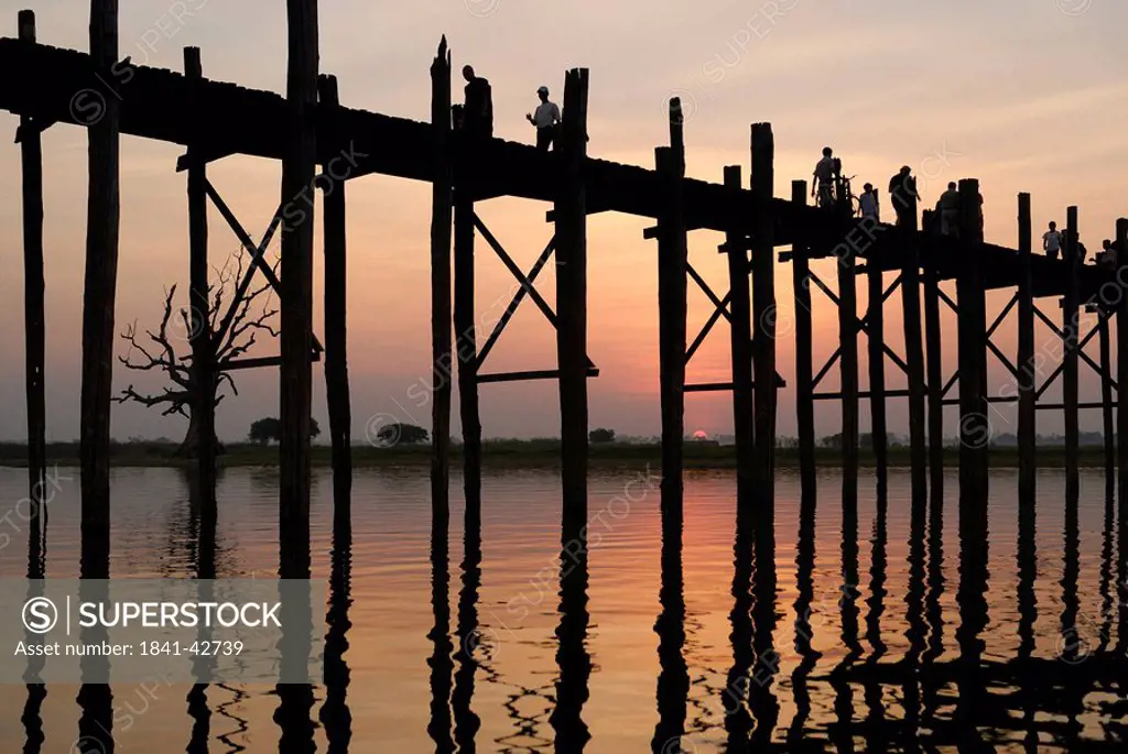 Silhouette of group of people walking on bridge across river at dusk, U Bein Bridge, Amarapura, Myanmar