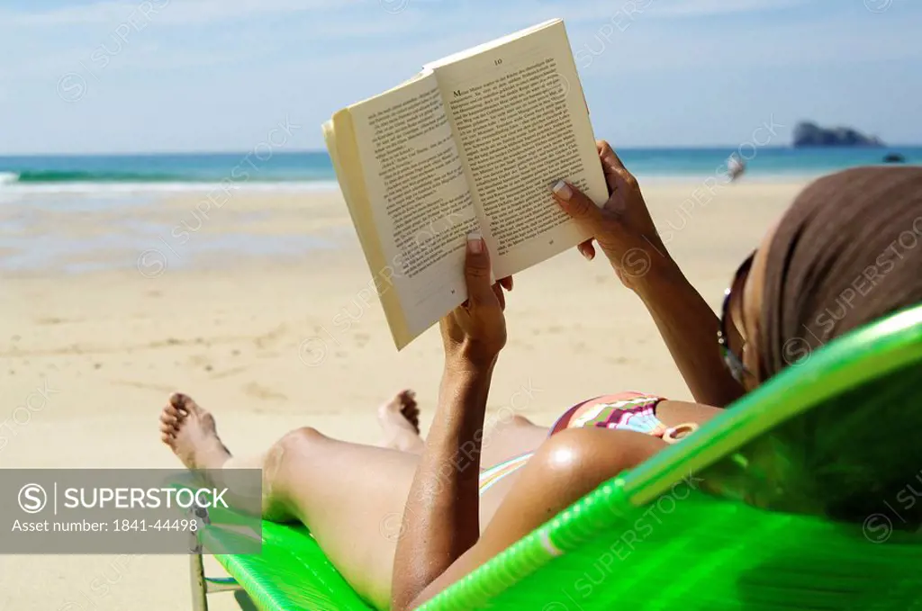 Rear view of woman reading book on beach chair