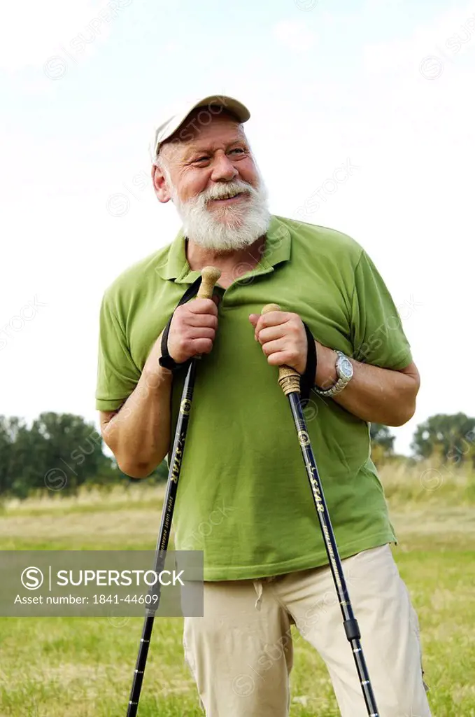 Mature man holding hiking poles and smiling in field