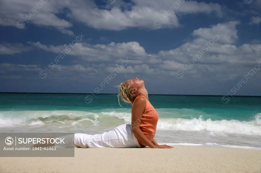 Woman practising yoga on a beach, side view