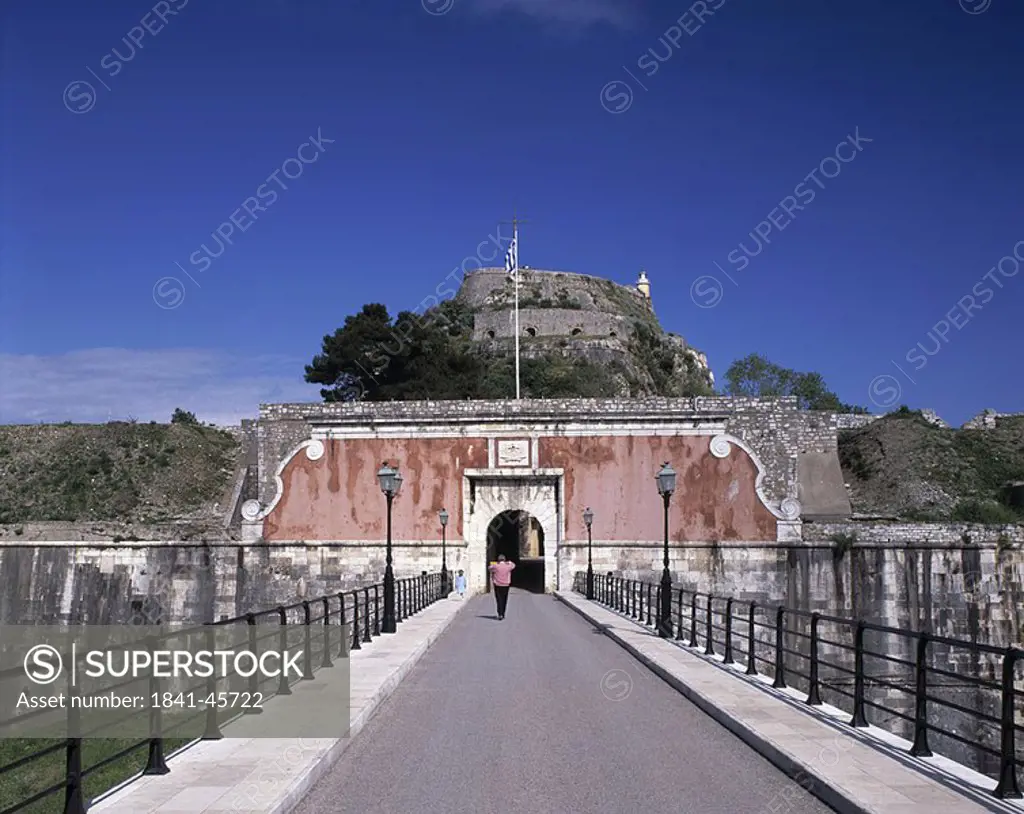 Person walking on bridge leading to archway of castle