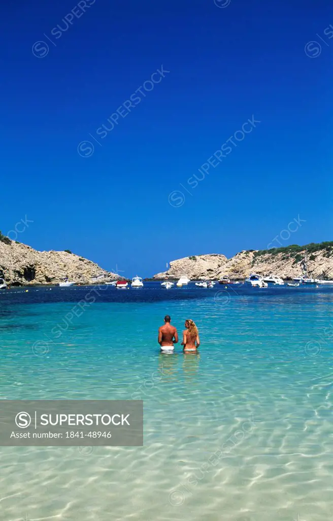 Rear view of couple standing in shallow water, Cala Moli, Ibiza, Balearic Islands, Spain