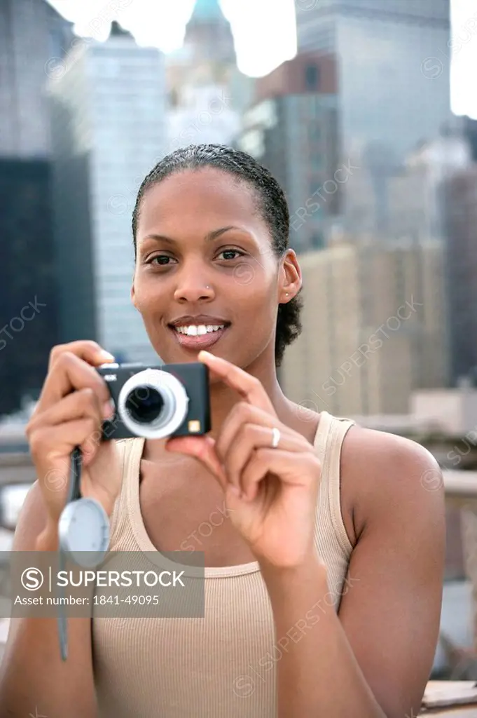 Woman holding a digital camera, skyline of New York in the background, USA