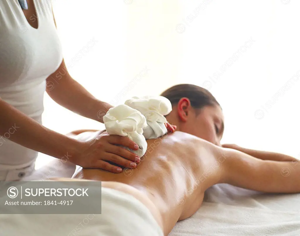 Rear view of naked young woman getting warming stone massage from massage therapist