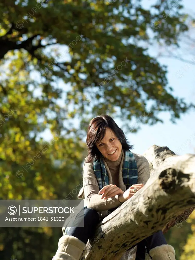 Portrait of mature woman sitting on fallen tree and smiling