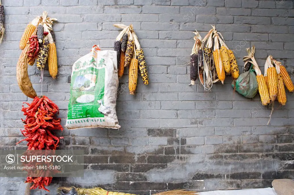 Strand of red chili peppers and bag hanging with corn cobs on wall, Pingyao, Shaanxi Province, China