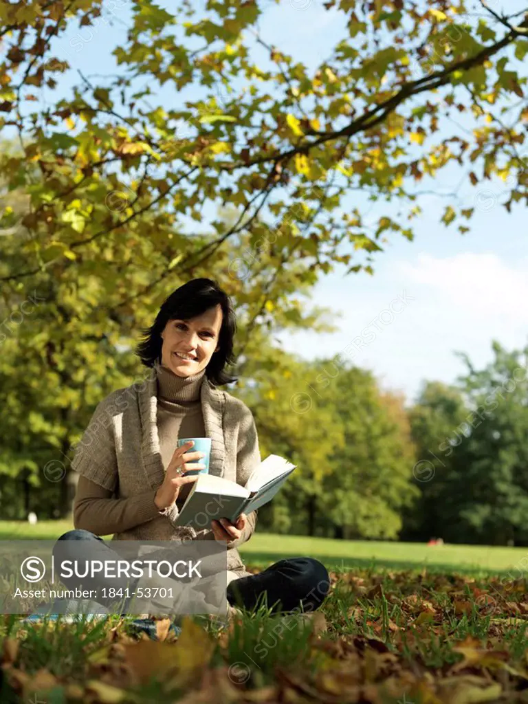 Portrait of mature woman holding book and smiling in park