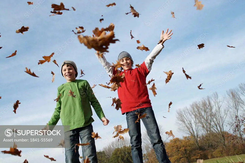 Low angle view of two boys throwing dry leaves