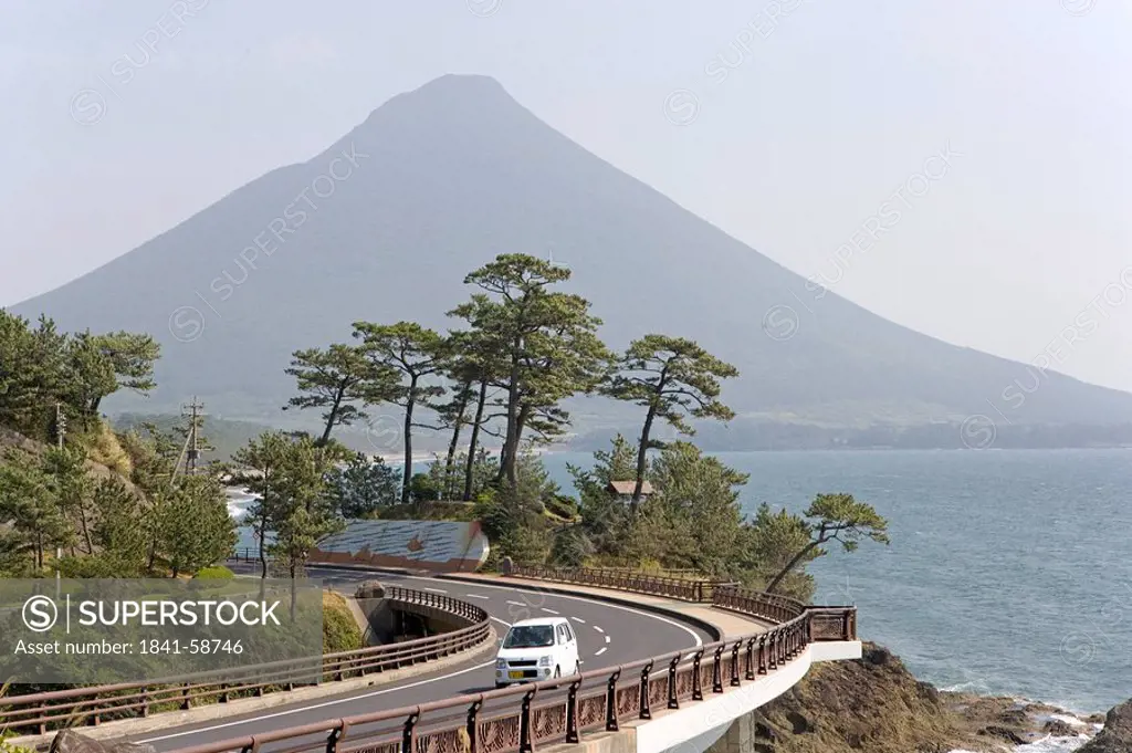 Car on a coastal road, volcano in the background, Ibusuki, Kyushu, Japan