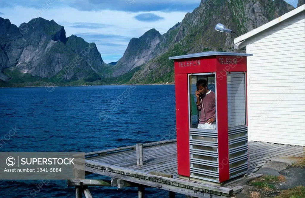 Person using the landline phone inside a telephone booth, Fjords, Norway