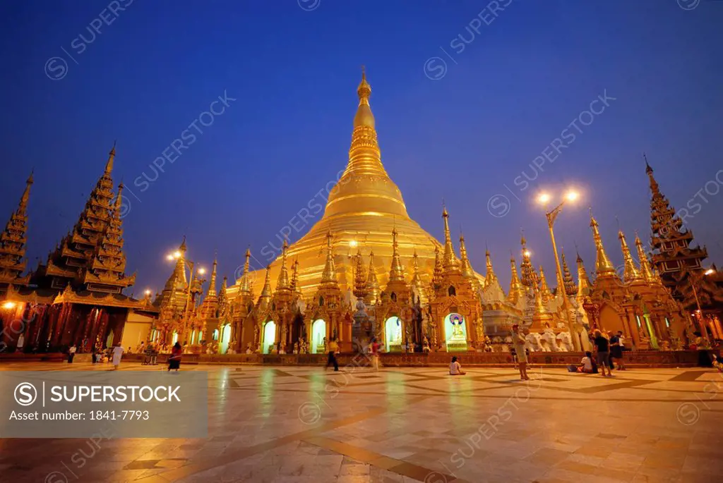 Group of people in Buddhist temple lit up at dusk, Shwedagon Pagoda, Yangon, Myanmar