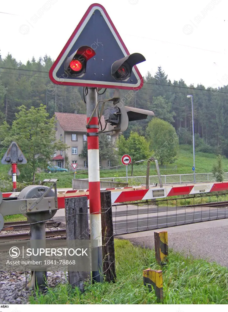 Closed railway crossing gate with lit up red light on post