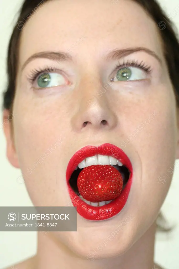 Young woman holding strawberry in mouth