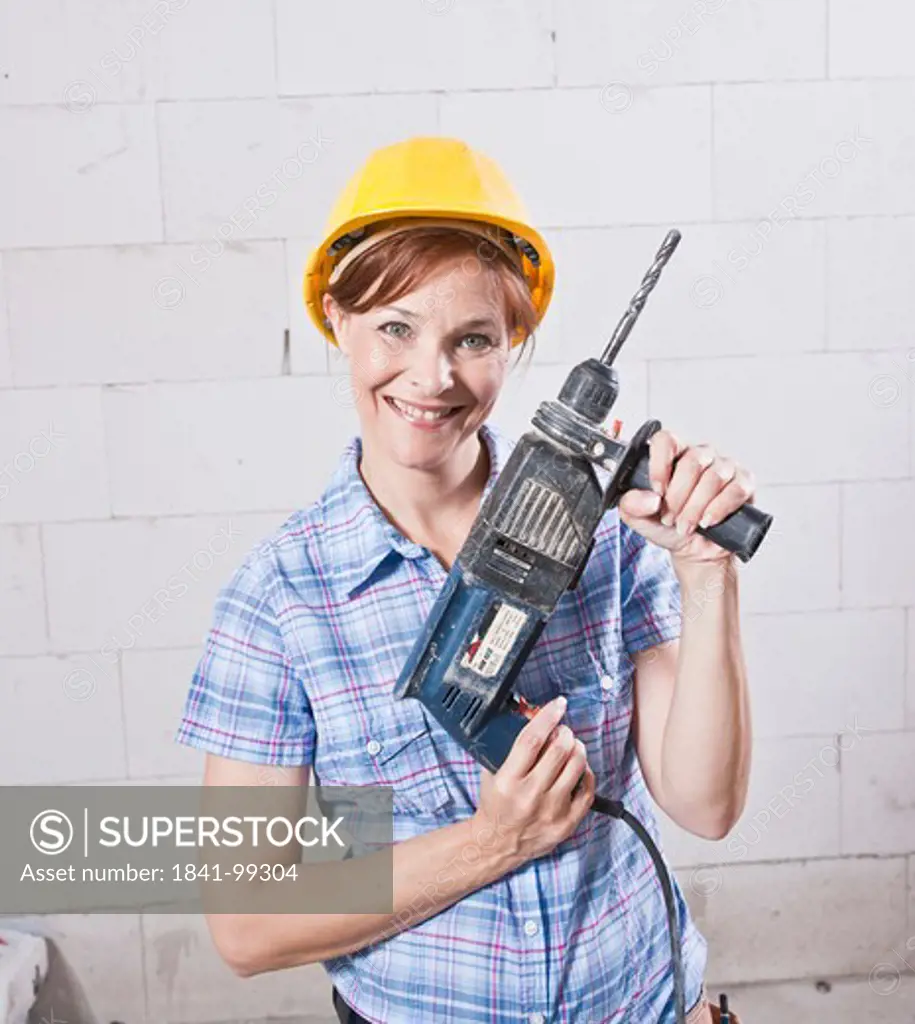 Smiling woman with helmet and drill